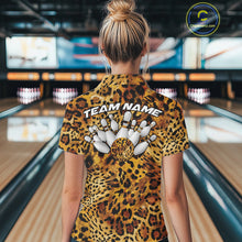 Load image into Gallery viewer, Back view of a woman standing at a bowling alley, wearing a gold, brown, and black leopard-print bowling polo with “Team Name” and bowling pins on the back.
