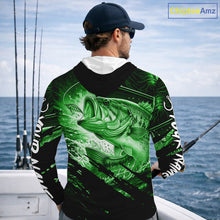 Load image into Gallery viewer, Person wearing a green and black bass hooded fishing shirt with a fish design, standing by the ocean.